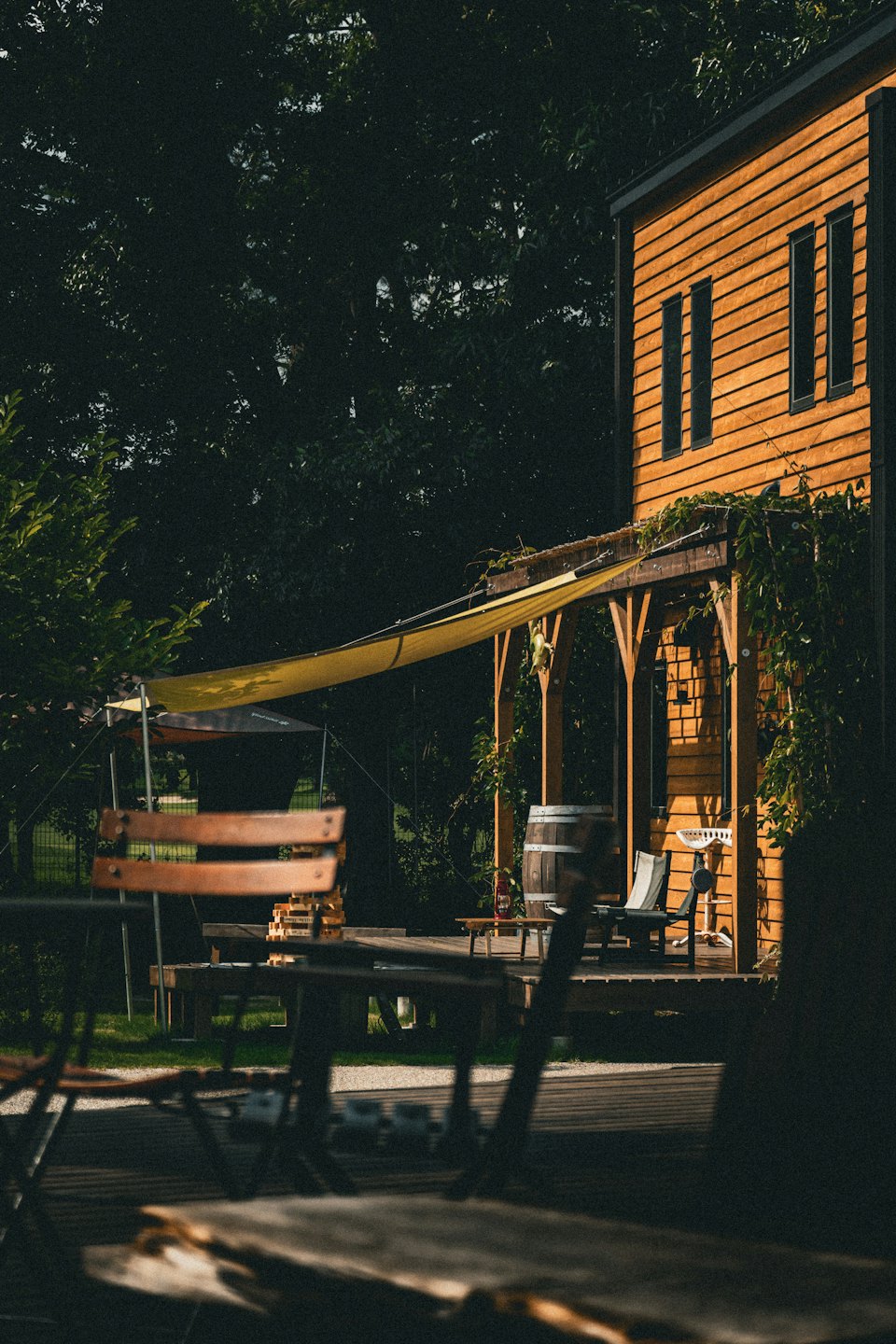 Wooden patio with a pergola and chairs beside a building.