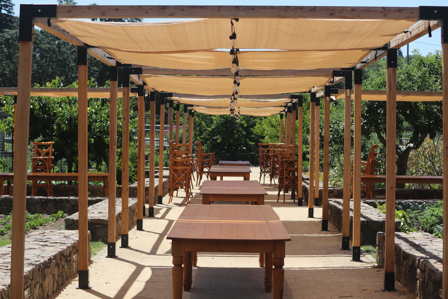 Empty outdoor dining area featuring wooden tables under a pergola.